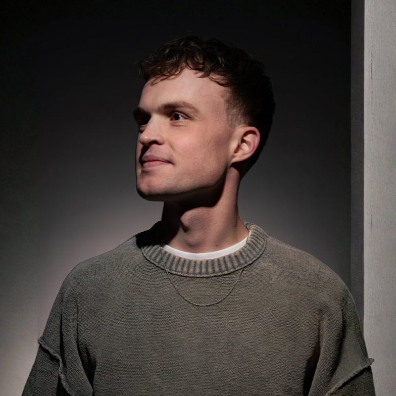 S3PPA, Dutch hard house and trance DJ, in a grey knit sweater with a thin chain, looking to the side